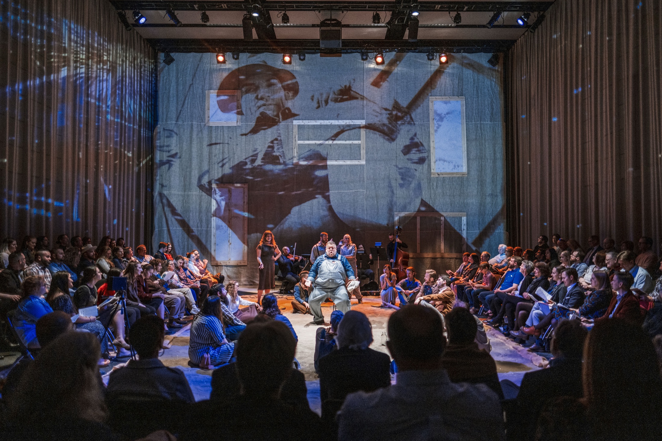 Dust Bowl performance with audience surrounding the stage and a large projection