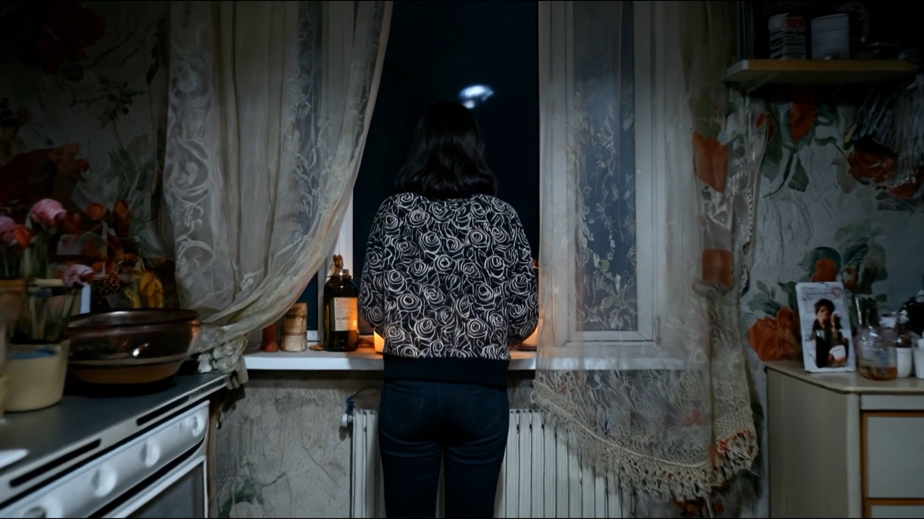 Still from Gurbet showing a figure looking out a kitchen window at night